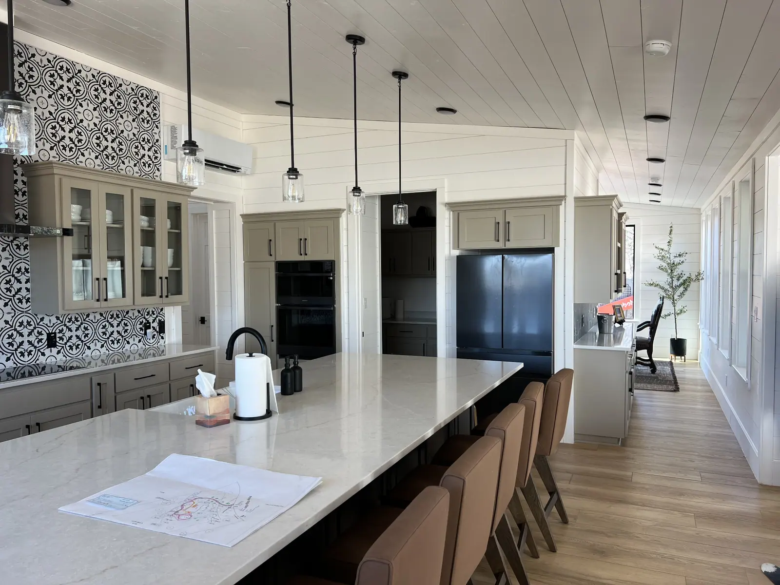 Long quartz island with bar seating, patterned tile backsplash and glass-front cabinetry
